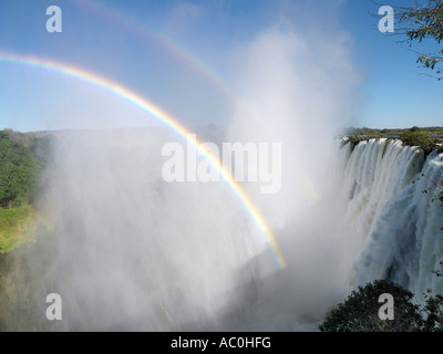 Ein doppelter Regenbogen über die Victoriafälle die Wasserfälle sind mehr als eine Meile breit und sind einer der weltweit größten Naturwunder der mächtigen Sambesi über 300 Fuß in einem donnernden brüllen mit Wolken von Spray Tropfen Stockfoto