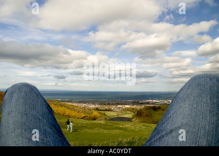 ein Blick von Arthurs Seat mit dem Meer im Blick durch ein paar Beine Stockfoto