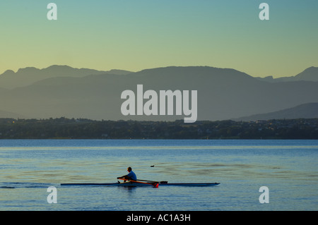 Rudern in den frühen Morgenstunden am Lac Leman, Schweiz, mit den französischen Alpen im Hintergrund. Stockfoto