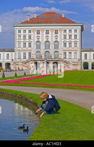 JUNGEN SPIELEN MIT ENTEN AUF DEM TEICH VOR SCHLOSS NYMPHENBURG MÜNCHEN BAYERN DEUTSCH Stockfoto