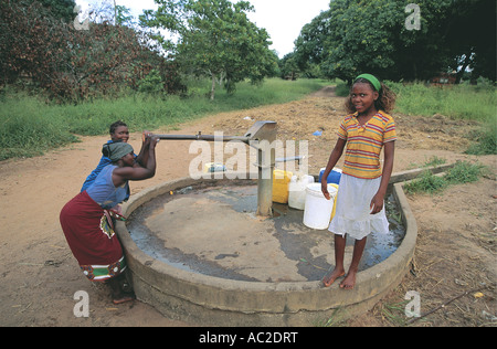 Frauen füllt Kunststoff Wasserbehälter aus einer Handpumpe in Mosambik, während ein hübsches Mädchen blickt auf Stockfoto