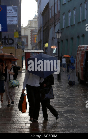 zwei junge Frauen, die Einkaufstaschen versteckt unter Dach entlang nass gepflasterten Straße während der Dusche Krakau Stockfoto