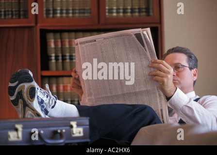 Rechtsanwalt mit Turnschuhen, Schreibtisch, Zeitung lesen Stockfoto