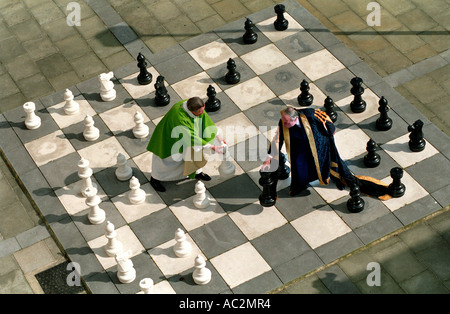 Menschlicher Ebene Schachbrett mit einem Herzog und Dekan in Roben mit riesigen Steinen spielend. Stockfoto