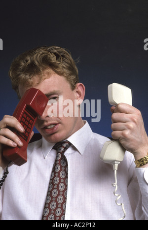 gestresst und überarbeitet Geschäftsmann versucht, zwei Telefone gleichzeitig im Büro sprechen Stockfoto