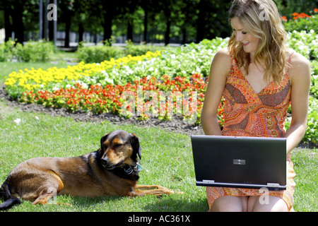 Haushund (Canis Lupus F. Familiaris), junge Frau trägt ein Sommerrock sitzen mit einem Notebook auf Rasen, Österreich Stockfoto