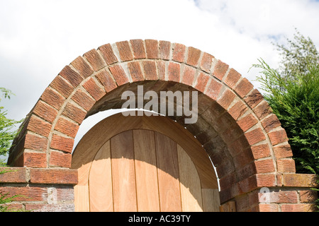 Gebogene rote Ziegelbogen über Garten Tor mit Holztür Woodmancote UK Stockfoto