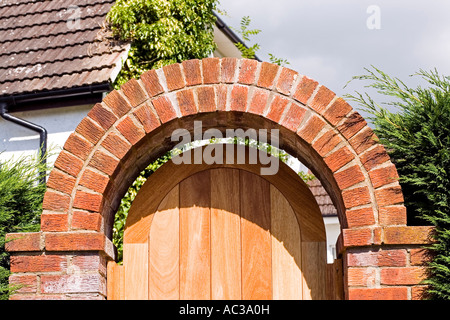 Gebogene rote Ziegelbogen über Garten Tor mit Holztür Woodmancote UK Stockfoto