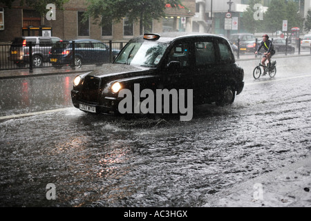 Ein Taxi Cab und Radfahrer finden ihren Weg entlang einer überfluteten Marylebone Road in London, während einer Sommer-Regen-Sturm Stockfoto