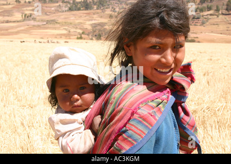 Quechua Landwirtschaft Mädchen mit bunten Schal mit kleinen Schwester festgeschnallt auf dem Rücken in Anden in der Nähe von Urubamba, Cuzco, Peru Stockfoto