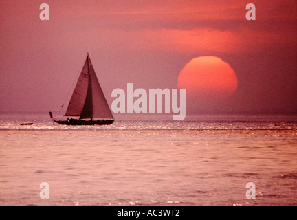 GROßE SONNE BEI SONNENUNTERGANG MIT YACHT SEGELN VORBEI AN ON SEA Stockfoto