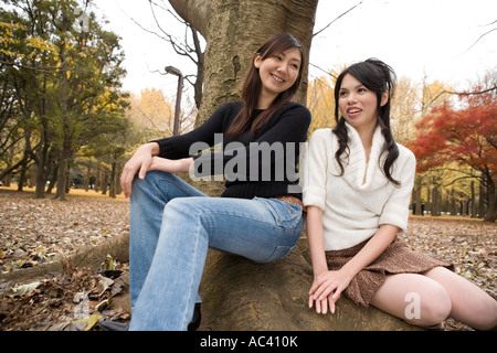 Zwei junge Frauen sitzen auf freiliegenden Wurzeln des Baumes Stockfoto