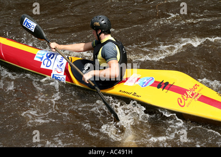 Ein Kajakfahrer manövriert durch das turbulente Wasser eines Flusses in Karlsbad und zeigt Können und Konzentration in einem hellgelben und roten Kajak. Stockfoto