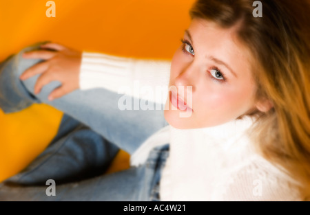 Schönes Teenager-Mädchen, das mit Händen am Bein sitzt und in die Kamera blickt, USA. Stockfoto