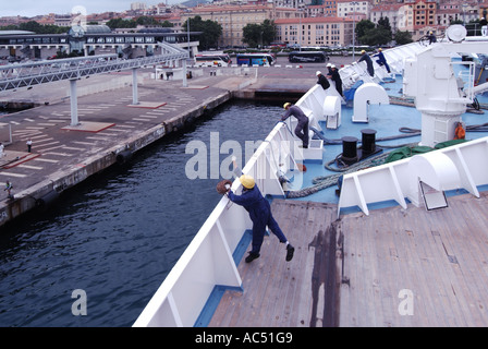 Kreuzfahrt-Liner-Andockverfahren Seemann wirft gewichtete Kugel und dünne starke Seil an Land, verbunden mit schweren Festmacherseilen, die von Hafenarbeitern zur Sicherung des Schiffes verwendet werden Stockfoto