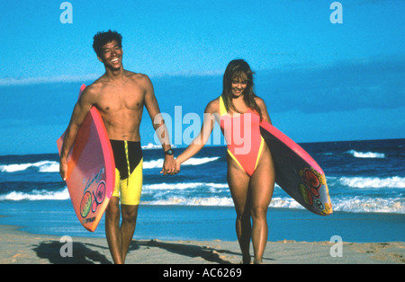 Hawaiian junge Paar mit Boogie-Boards, die hand in hand gehen, entlang des Strandes Oahu Hawaii USA Stockfoto