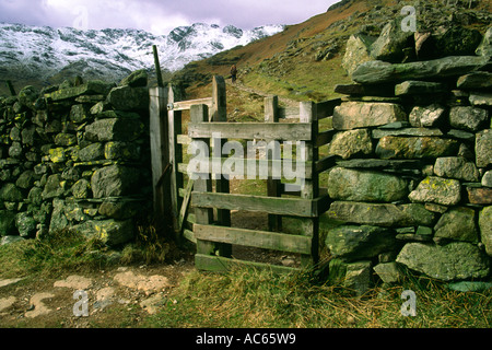 Ein küssen Tor auf der Band und einer Steinmauer mit Schnee gekrönt Crinkle Crags Hügeln im Hintergrund Stockfoto