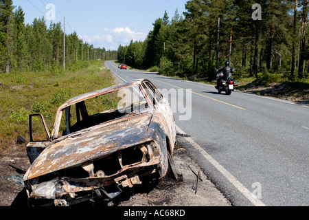 Verbrannt Volvo Limousine an Landstraße. Motorradfahrer und vorbeifahrende Autos, Finnland Stockfoto