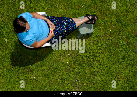 Eine Frau aufstellen ihre Füße mit einer Tasse Tee auf einer Wiese mit Gänseblümchen. Platz für Text auf dem Rasen. Stockfoto