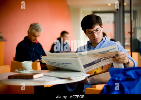 Mann liest Zeitung the Guardian in Aberystwyth Arts Centre Cafe auf dem Campus der Universität Stockfoto