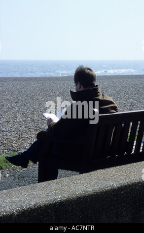 Mann sitzt auf der Bank durch das Meer lesen im Vereinigten Königreich Stockfoto