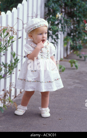 Babymädchen stehen von weißen Lattenzaun in liebenswert Kleid und Hut Stockfoto