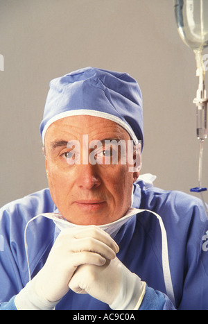 Ein Braunhaarige Mann tragen Blau medizinische Peelings Schutzhandschuhe Maske um Hals stützte sich auf seine gefalteten Hände Stockfoto