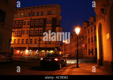 Nachtblick auf eine ruhige Straße in Prag mit historischen Gebäuden, die von Straßenlaternen beleuchtet werden, und einem Auto, das auf der Kopfsteinpflasterstraße parkt. Stockfoto