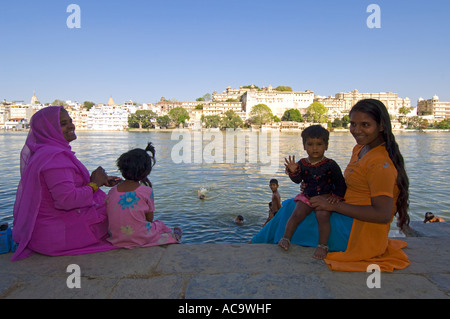 Lokale Leute versammeln sich an den Ghats zu waschen, Schwimmen und erfrischen Sie sich im Pichola-See mit dem Stadtschloss im Hintergrund. Stockfoto
