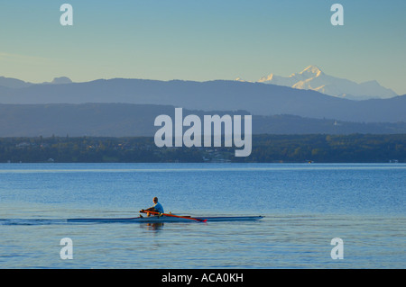 Rudern in den frühen Morgenstunden am Lac Leman, Schweiz, mit den französischen Alpen im Hintergrund. Stockfoto