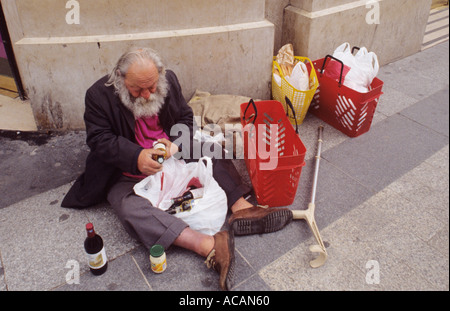 Alkoholloser, obdachloser älterer Mann, der im Stadtzentrum auf dem Bürgersteig mit Weinflaschen sitzt. Stockfoto