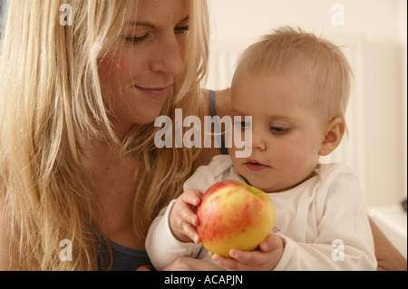 Junge blonde Mutter mit einem Kleinkind hält einen Apfel Stockfoto