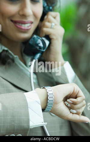 Eine Geschäftsfrau mit Blick auf ihre Armbanduhr und sprechen auf einer Telefonzelle in Nahaufnahme Stockfoto