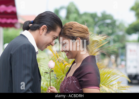 Seitenansicht einer jungen Frau hält eine Rose und mit Blick auf einen Mitte erwachsenen Mann Stockfoto