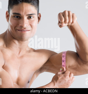 Porträt eines jungen Mannes, der seinen Bizeps mit einem Maßband messen Stockfoto