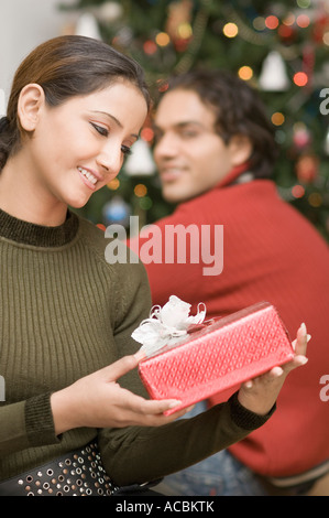 Nahaufnahme einer jungen Frau, Blick auf ein Weihnachtsgeschenk mit einem jungen Mann neben ihr sitzen Stockfoto