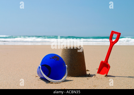 Sandburg mit roten Spaten und blauen Eimer am Sandstrand Stockfoto