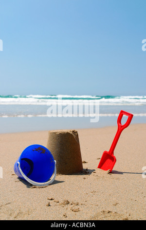 Sandburg mit roten Spaten und blauen Eimer am Sandstrand Stockfoto