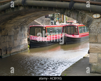 Zwei rot bemalten schmalen Kanalboote unter eine gewölbte Brücke am Leeds-Liverpool-Kanal in Skipton West Yorkshire gesehen Stockfoto