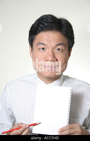 junger Mann von chinesischer Abstammung hält einen leeren Notizbuch und Stift Stockfoto