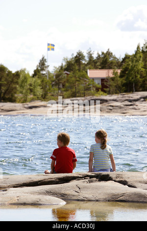 Zwei Kinder sitzen auf einer Klippe in den Schären. Stockfoto