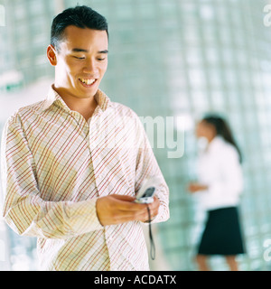 Ein Mann mit einem Lächeln auf den Lippen einer Frau im Hintergrund Handy beschäftigt. Stockfoto