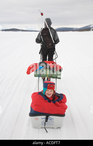 Rodeln in Lappland: eine Mädchen sitzt in einem "Pulka" ist von der Mutter über den zugefrorenen See Holmajarvi gezogen Stockfoto