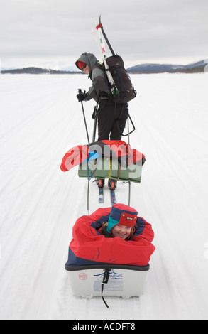 Rodeln in Lappland: eine Mädchen sitzt in einem "Pulka" ist von der Mutter über den zugefrorenen See Holmajarvi gezogen Stockfoto