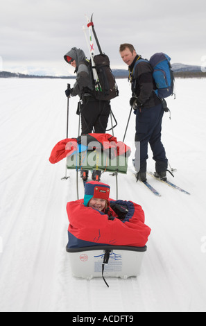 Rodeln in Lappland: eine Mädchen sitzt in einem "Pulka" ist von ihren Eltern über den zugefrorenen See Holmajarvi gezogen Stockfoto