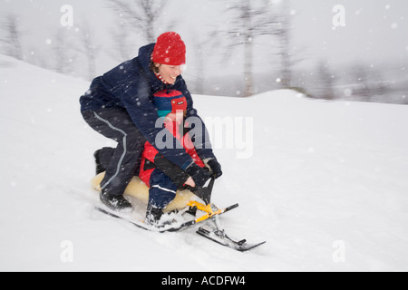 Rodeln in Lappland: ein Mädchen auf einem Schnee-Racer mit ihrer Mutter im Schneetreiben einen Hügel hinunter fahren. Stockfoto