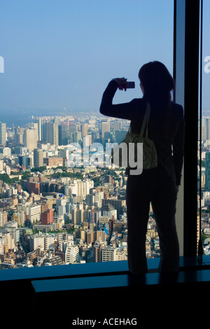 Silhouette der Frau ein Panoramafenster mit Blick und ein Foto von Tokio mit ihrem Handy Stockfoto