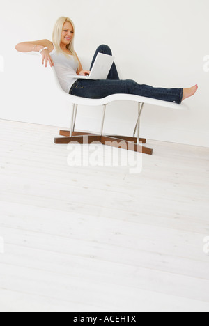 junge Frau mit Laptop auf moderne Stuhl sitzend Stockfoto