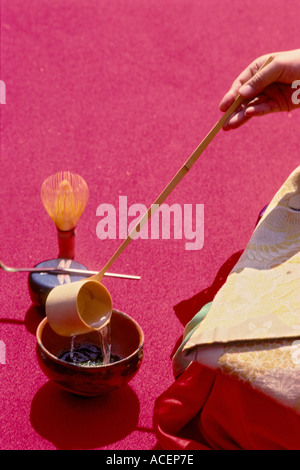 Eine Frau im Kimono gießt heißes Wasser in eine Tasse mit einem Bambus-Schöpflöffel während einer japanischen Teezeremonie Stockfoto