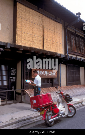 Postbote mit einem roten Motorrad, um Post in einem Machiya Stadthaus in Kyoto, Japan, zu liefern. Stockfoto